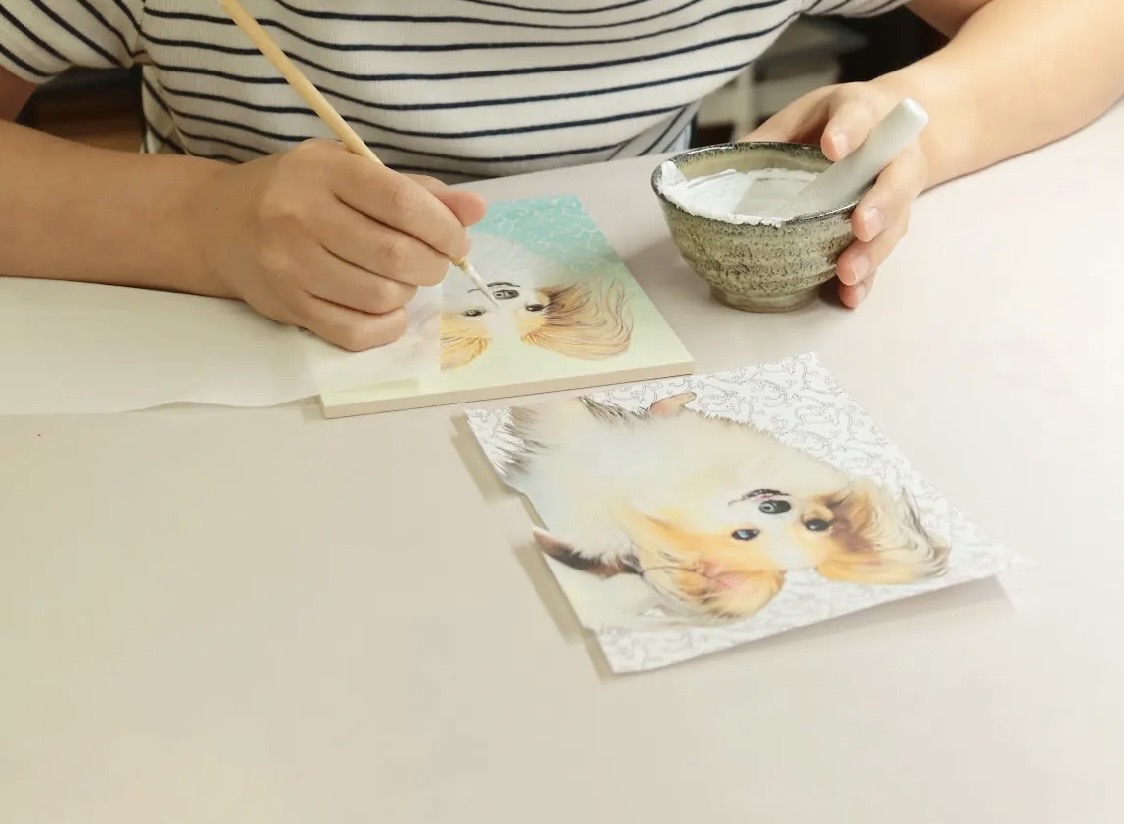 両腕と手元を写した、犬の姿を陶板に絵付けする作家
